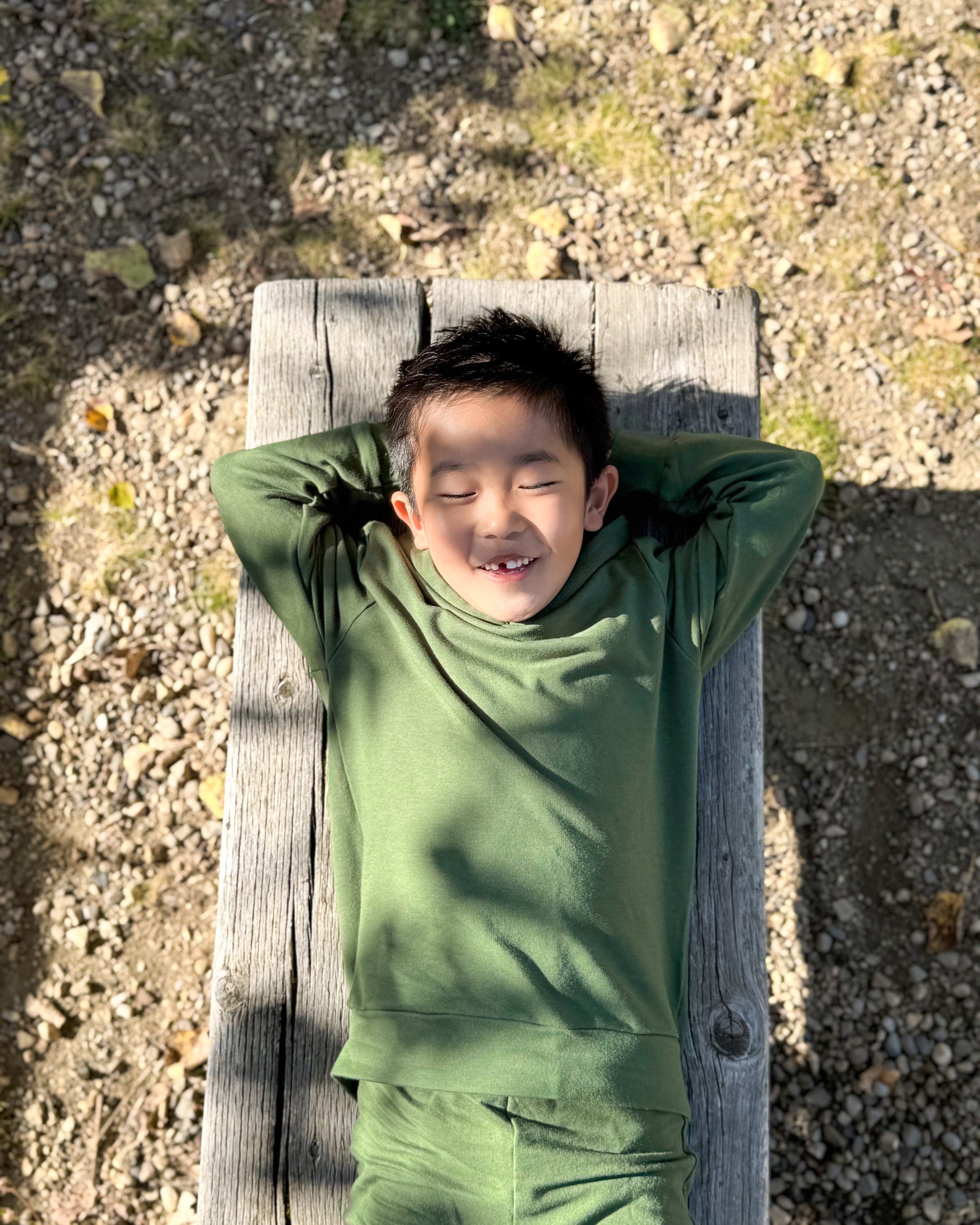 Child in green outfit lying on a wooden plank outdoors