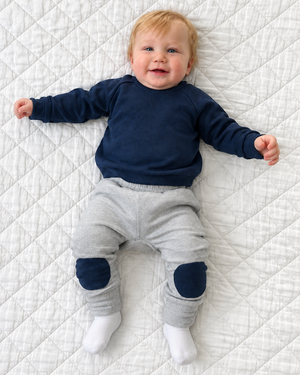 Boy in a navy sweater and grey pants with both feet in white socks