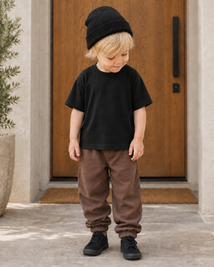 Boy in black sneakers, relaxed brown sweatpants and a slightly longer black tee