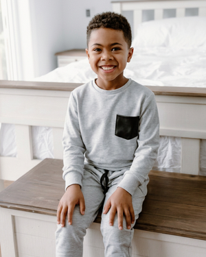 Boy sitting upright on the bench in his grey pocket crewneck
