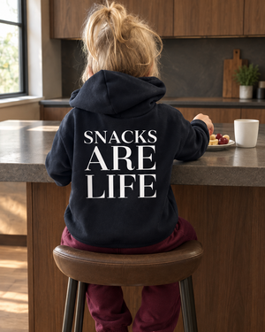 Girl having a snack at a moody kitchen island wearing a Snacks Are Life hoodie and burgundy pants