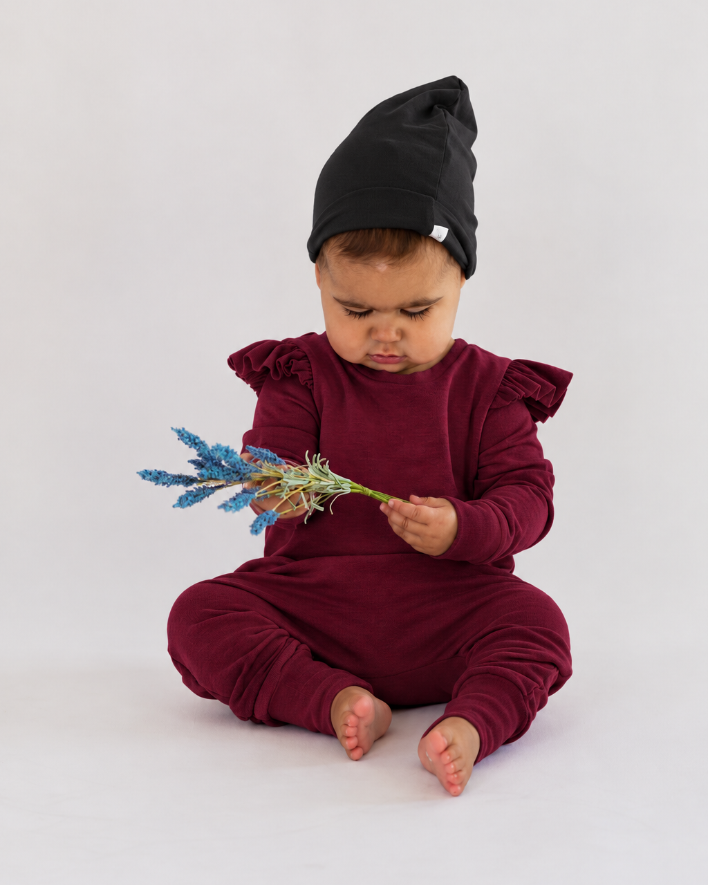Little girl in a burgundy ruffle romper and black toque