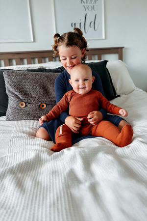 Older sister in a navy long-sleeved dress holding her baby sibling