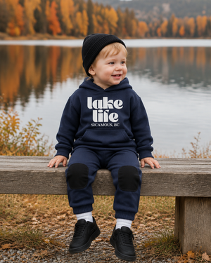 Regenerated boy sitting on a lakeside bench in a navy Lake Life outfit