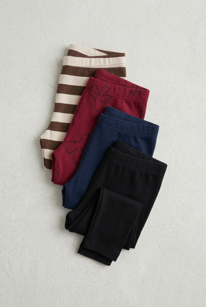 Stacked leggings in brown stripe, burgundy bows, navy, and black on a light concrete background