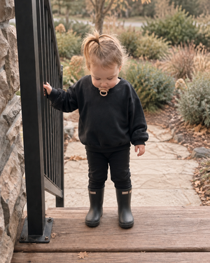 Toddler standing at the top of porch stairs looking down and holding the railing