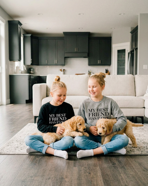 Two sisters sitting with goldendoodle puppies in matching paws crewnecks